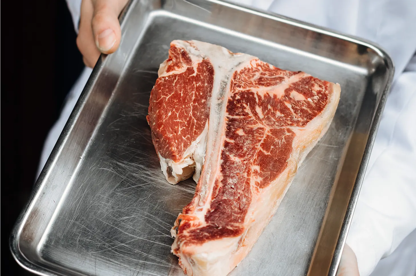 Raw T-bone steak on a metal tray.